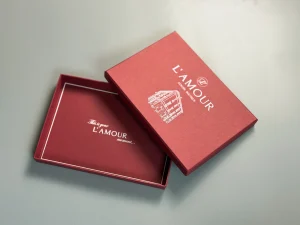 Відкрита бордова коробка L’AMOUR з написом усередині та кришкою з білим малюнком