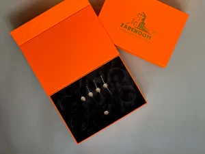 Відкрита помаранчева коробка ZARENDOM на магнітах з чорним ложементом і виробами